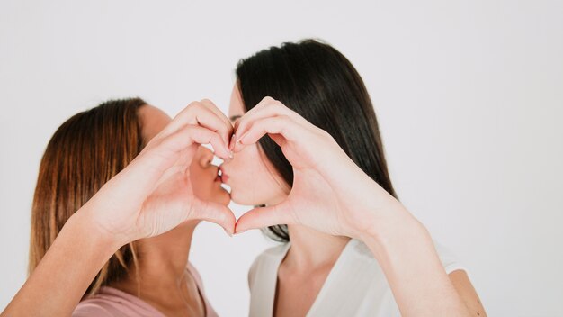 Lesbian couple kissing and gesturing heart