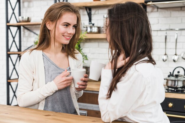 Lesbian young couple holding cup of coffee in hand looking at each other