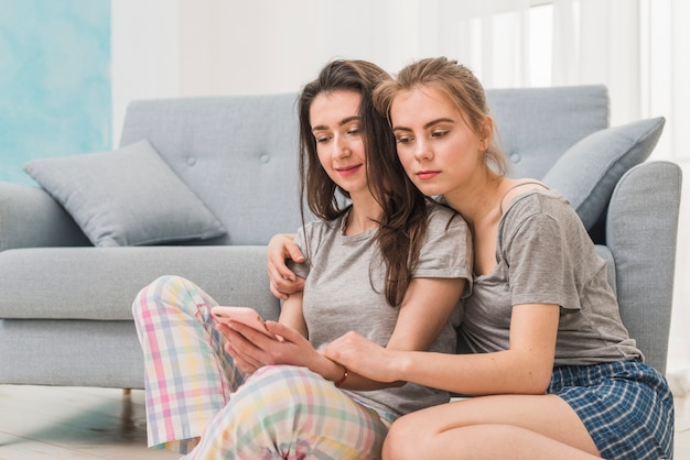 Free photo lesbian young couple sitting near the sofa using mobile phone at home