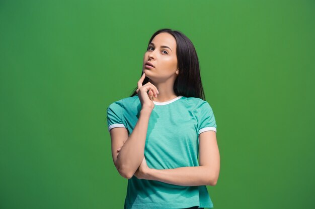 Let me think. Doubt concept. Doubtful pensive woman with thoughtful expression making choice. Young emotional woman. Human emotions, facial expression concept. Front . Studio. Isolated on trendy green