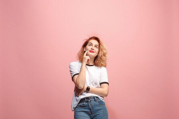 Let me think. Doubtful pensive woman with thoughtful expression making choice against pink wall