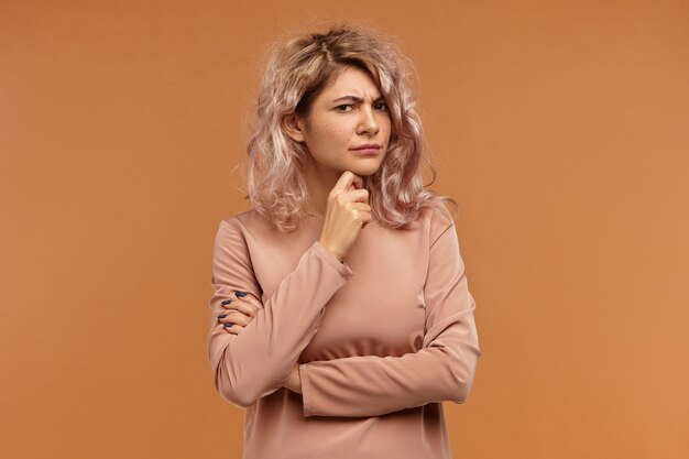 Let me think. Picture of frowning serious young woman with pinkish hair holding hand on her chin, having concentrated pensive facial expression
