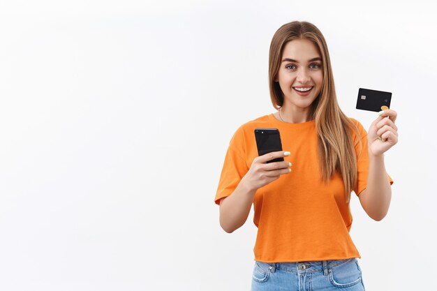 온라인 쇼핑을 해보자. 코비드-19 자가 격리에 앉아 신용 카드와 휴대 전화를 사용하여 음식 배달 비용을 지불하는 쾌활한 금발 소녀의 초상화
