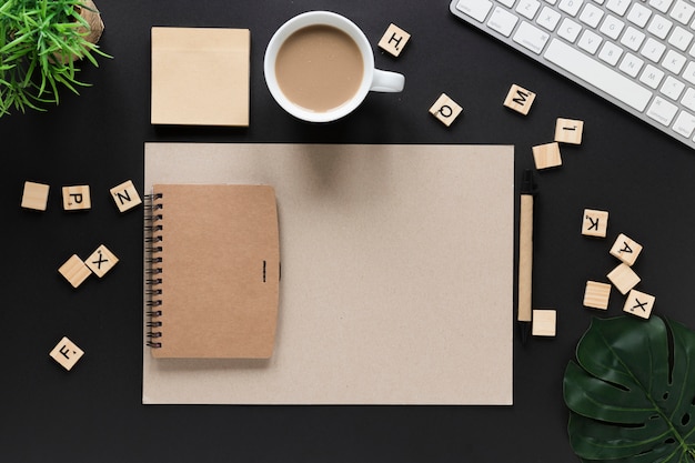 Letter wooden blocks; tea cup; sticky note; diary; card paper and keyboard on black desk