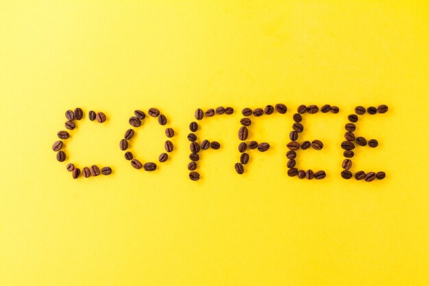 Letters Coffee Beans on yellow vibrant background. Minimalism Food Morning Energy Concept. 
