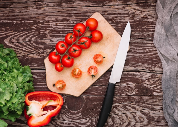 Lettuce; bell pepper and cherry tomatoes on chopping board with knife over the wooden desk