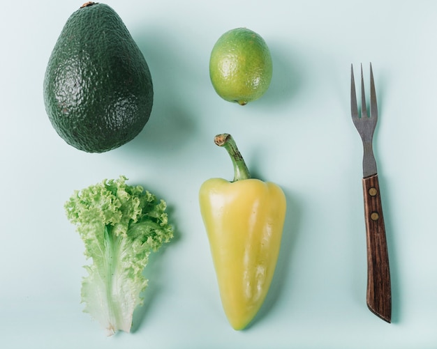 Lettuce; lemon; avocado and bell pepper near fork on green surface