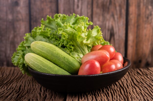 Lettuce, tomatoes, and cucumber in a black bowl on the wooden floor.