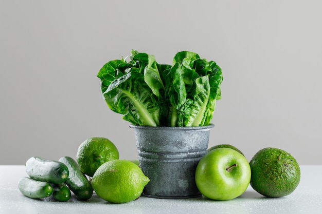 Lettuce with cucumber, lime, apple, avocado in a mini bucket on white and grey table