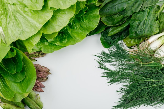 Lettuce with spinach, asparagus, sorrel, green onions and pods, dill high angle view on a white wall