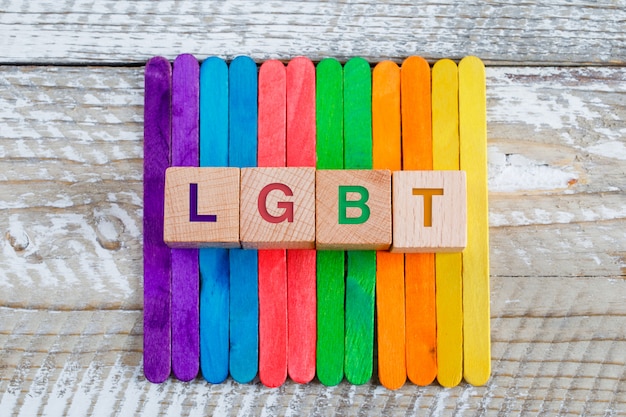 Lgbt concept with colored ice cream sticks, wooden cubes on wooden background flat lay.