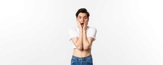 Lgbtq and pride concept Image of surprised androgynous guy gasping amazed and staring at camera in awe standing over white background