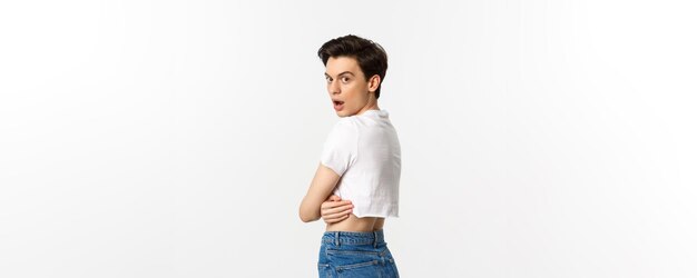 Lgbtq and pride concept Side view of surprised gay man open mouth in awe staring at camera turn head at you while standing in profile in crop top white background