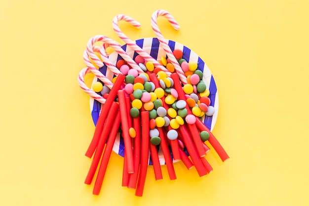 Licorice, gems and christmas cane candies on plate over the yellow backdrop