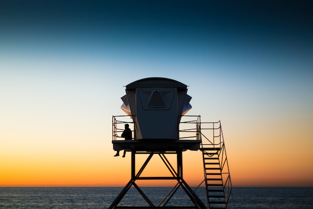 Foto gratuita bagnino in spiaggia sulla torre di guardia al tramonto