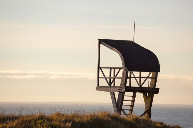 Lifeguard tower in a field surrounded by the sea under a cloudy sky in the evening