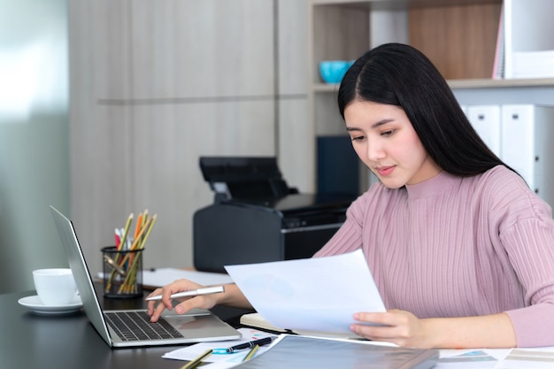 ライフスタイル美しいアジアビジネス若い女性のオフィスの机の上のラップトップコンピューターとスマートフォンを使用して