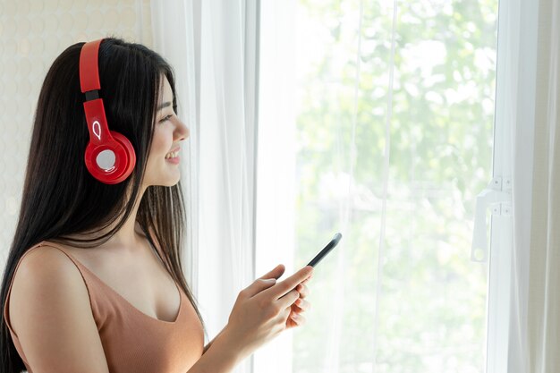 ライフスタイル美しいアジアの女性かわいい女の子は幸せを感じる白い寝室のイヤホンヘッドフォンで音楽を聴くを楽しむ
