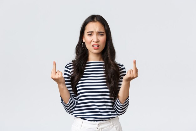 Lifestyle, beauty and fashion, people emotions concept. Annoyed pissed-off asian woman stare bothered and displeased, showing middle-fingers careless what people say, white background