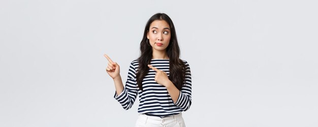 Lifestyle beauty and fashion people emotions concept Curious and interested cute asian girl peeking and pointing fingers left at new promo banner with special discount in shop
