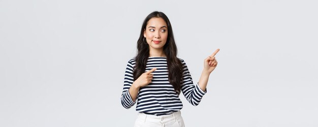 Lifestyle beauty and fashion people emotions concept Intrigued stylish young asian woman looking and pointing at right banner with pleased tempting expression wants buy something