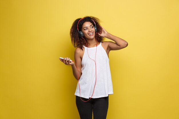 ライフスタイルの概念 - 携帯電話で音楽を聴いて楽しい美しいアフリカ系アメリカ人女性の肖像画。黄色のパステルスタジオの背景。スペースをコピーします。