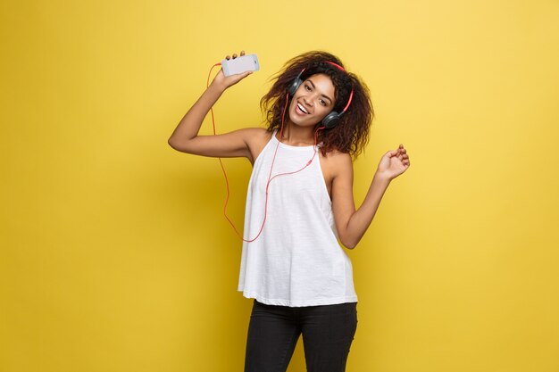 Lifestyle Concept - Portrait of beautiful African American woman joyful listening to music on mobile phone. Yellow pastel studio background. Copy Space.