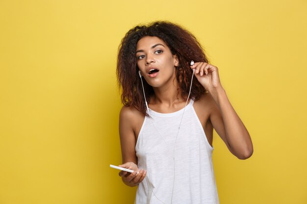 Lifestyle Concept - Portrait of beautiful African American woman joyful listening to music on mobile phone. Yellow pastel studio background. Copy Space.