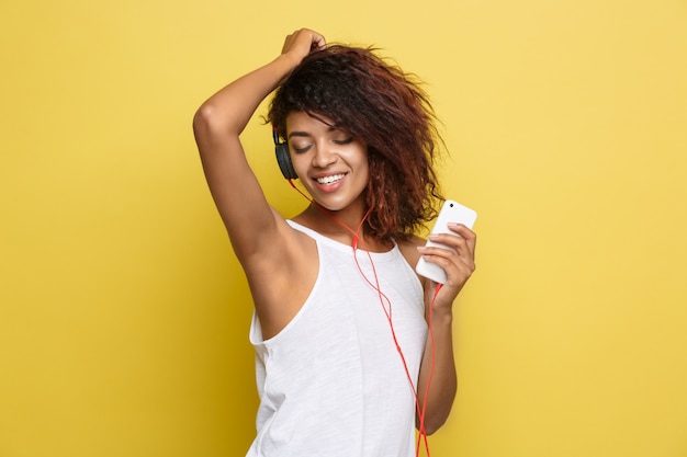 Lifestyle Concept - Portrait of beautiful African American woman joyful listening to music on mobile phone. Yellow pastel studio background. Copy Space.