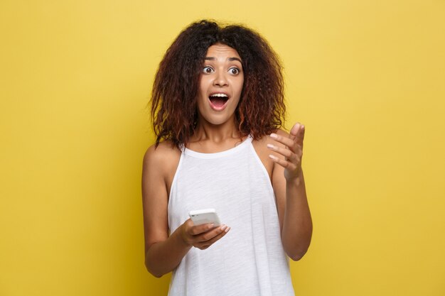 Lifestyle Concept - Portrait of beautiful African American woman shocking with something on mobile phone. Yellow pastel studio background. Copy Space.