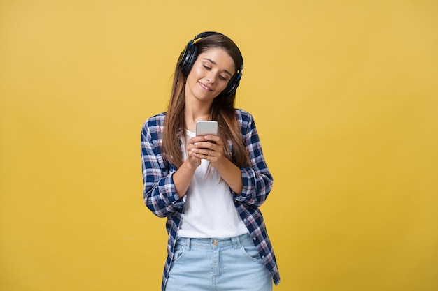 Free photo lifestyle concept portrait of beautiful caucasian woman joyful listening to music on mobile phone yellow pastel studio background copy space