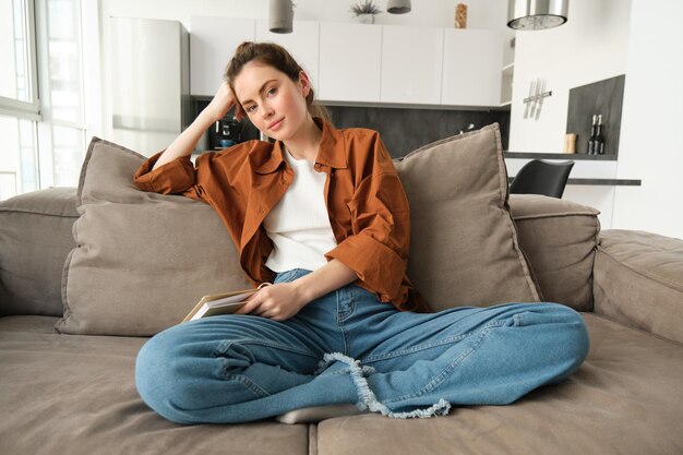 Free photo lifestyle concept young smiling brunette woman sitting at home on sofa resting on couch looking at