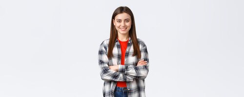 lifestyle different emotions leisure activities concept cheerful young caucasian girl female student in checked casual shirt cross arms chest and demiling pleased standing white background