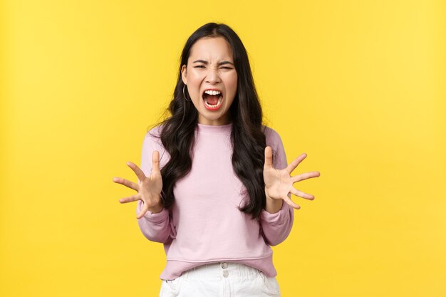 Lifestyle, emotions and advertisement concept. Mad and distressed korean girl losing temper, feeling angry and overwhelmed, screaming and shaking hands aggressive, standing yellow background.
