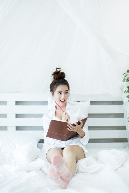 Lifestyle happy young Asian woman enjoying lying on the bed reading book at home.