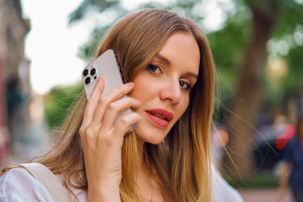 Lifestyle outdoor portrait of pretty blonde woman speaking by her smatphone.