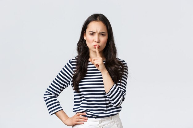 Lifestyle, people emotions and casual concept. Angry serious young asian woman scolding person being loud, shush with mad face and index finger pressed to lips, tell be quiet