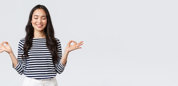 Lifestyle people emotions and casual concept Calm happy young woman feeling peaceful during meditation close eyes and smiling as hold hands in zen nirvana gesture do yoga exercise