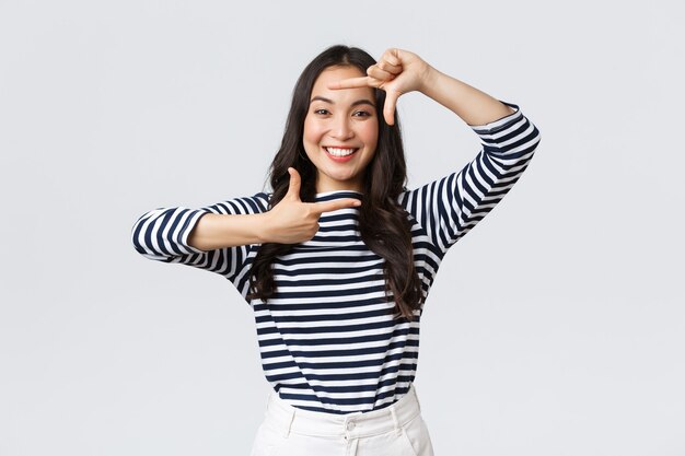 Lifestyle, people emotions and casual concept. Creative cute asian girl picturing, capture moment with hand frames gesture, smiling amused, staying positive and happy, white background