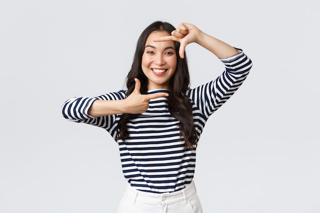 Lifestyle, people emotions and casual concept. Creative cute asian girl picturing, capture moment with hand frames gesture, smiling amused, staying positive and happy, white background