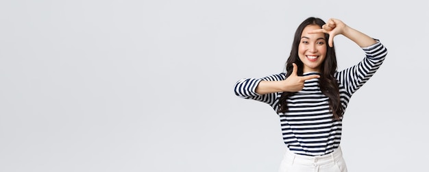 Lifestyle people emotions and casual concept Creative cute asian girl picturing capture moment with hand frames gesture smiling amused staying positive and happy white background