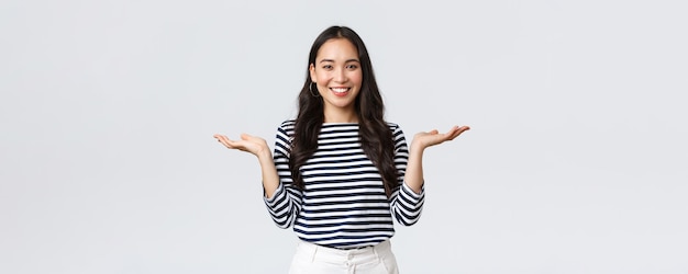 Lifestyle people emotions and casual concept Cute smiling asian woman introduce two products hold hands sideways as if demonstrating products on palms standing white background