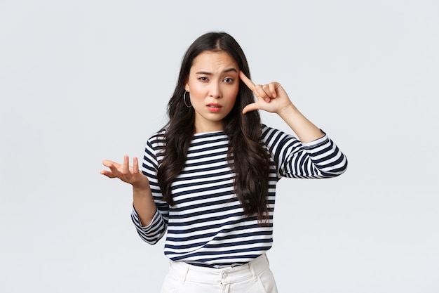 Lifestyle, people emotions and casual concept. Disappointed and annoyed young asian woman scold person making stupid mistake, roll finger over temple and raise hand in dismay