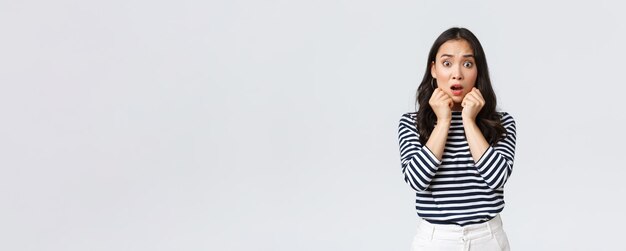 Lifestyle people emotions and casual concept Scared worried asian girl in striped shirt gasping looking alarmed got in trouble find out shocking truth standing white background