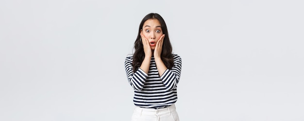 Lifestyle people emotions and casual concept Surprised gasping woman stare impressed losing speech from emotions drop jaw and touch face amazed standing white background