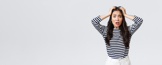 Lifestyle people emotions and casual concept Troubled young woman stare alarmed feel bad as something awful happened grab head and stare camera anxious white background