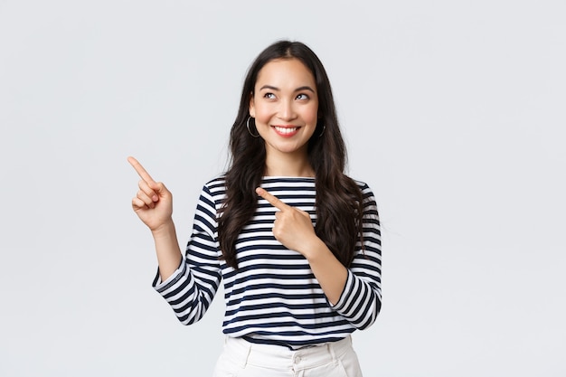 Lifestyle, people emotions concept. Excited good-looking asian girl smiling pleased as found excellent product, pointing fingers left at advertisement and looking satisfied, recommend promo