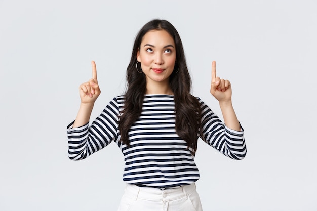 Lifestyle, people emotions concept. Excited good-looking asian girl smiling pleased as found excellent product, pointing fingers up at advertisement and looking satisfied, recommend promo