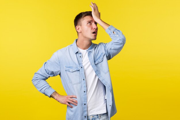 Lifestyle, people emotions and summer leisure concept. Annoyed and tired blond guy punch himself in forehead and roll eyes bothered, exhausted explaining something, yellow background.