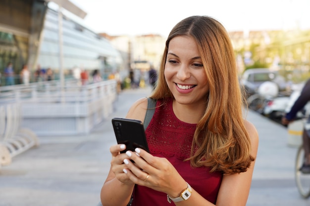 Lifestyle portrait of business woman on evening city using smartphone app, casual girl typing text message on mobile device outdoors
